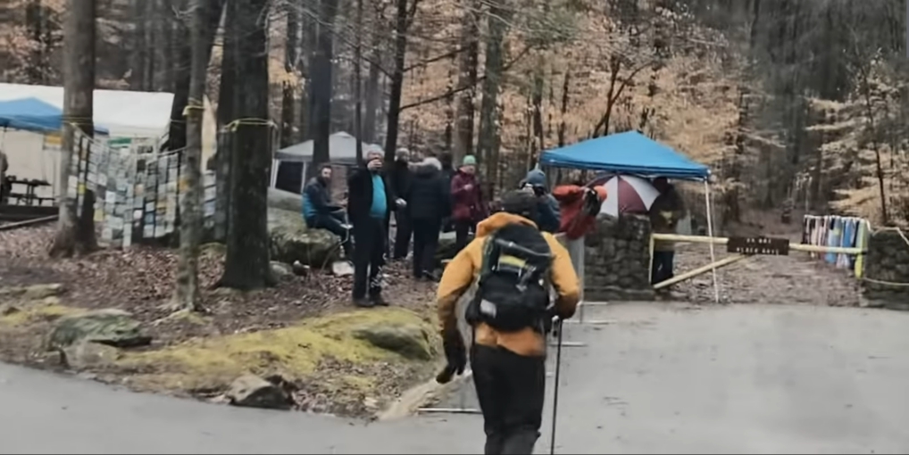 A woman in orange, Jasmin, running down a road into a camp.