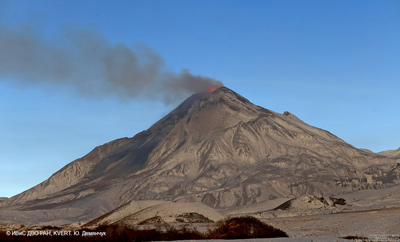 A volcano emitting a plume of ash, with the orange glow of lava around its summit