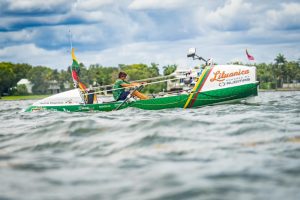 a green rowing boat near a forested shore