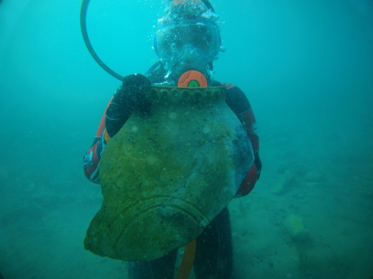 A diver underwater holding a ceramic fragment.