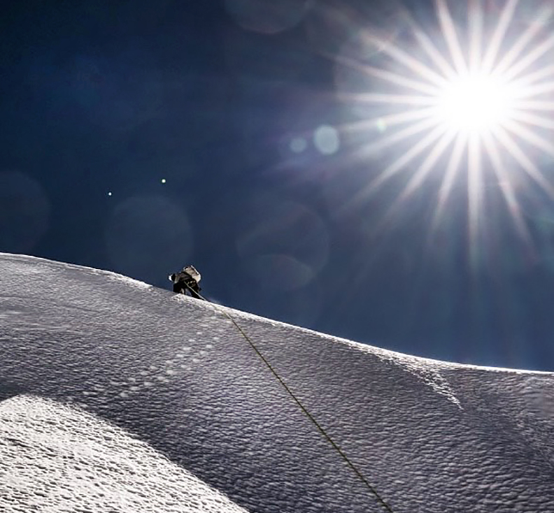 A climber on a snow ridge under the sun.