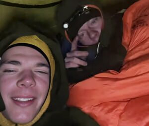 Two climbers dressed in warm clothes inside a tent.