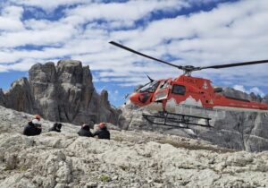 a helicdopter drops two people on a flat summit in the Dolomites.