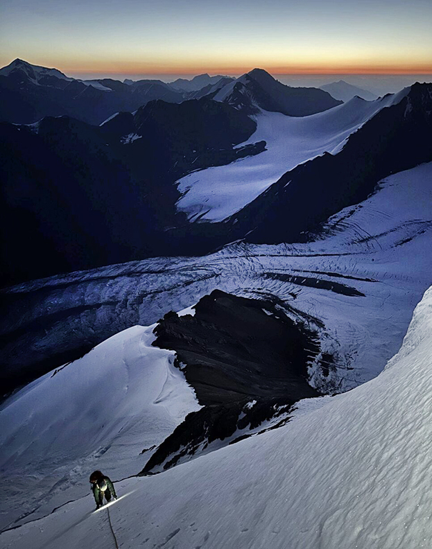 climber with headlamp goes up twilit peak