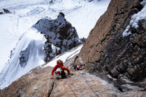 Two climbers ona granite wall, snowy glaciers at their feet.
