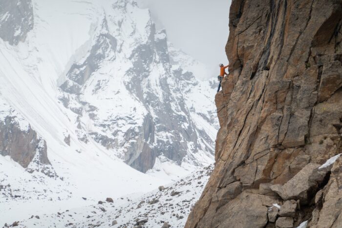 A climber on a rock face with a big snowy peak in background in a foggy day.