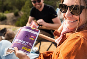 A woman eats the Good To-Go Mushroom Risotto with friends while camping