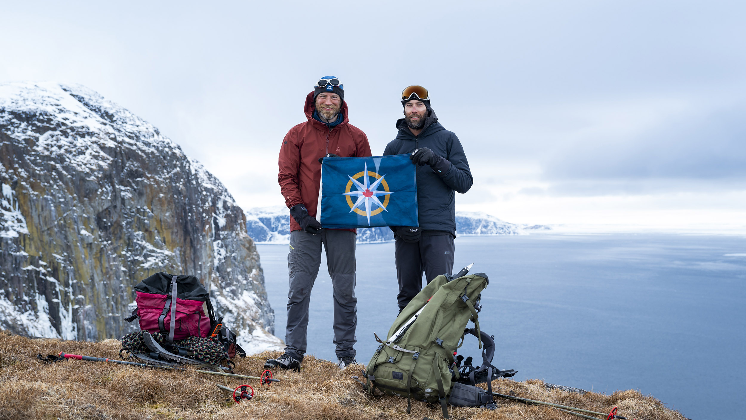 two men stand on a cliff holding a flag