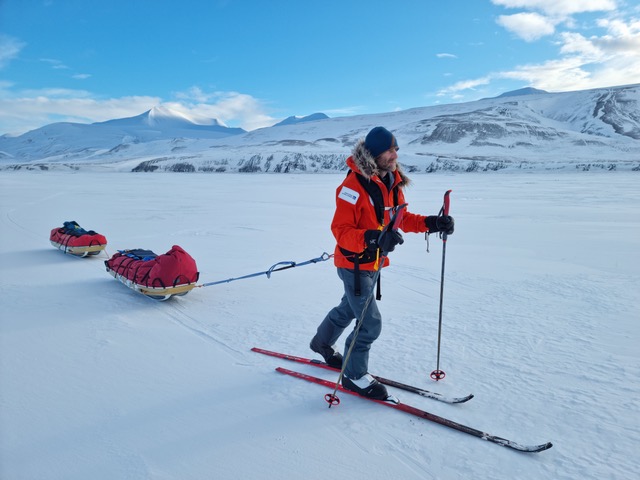 A man on skis drags two sleds behind him over the snow.