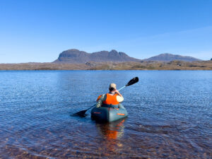 Man paddles packraft on calm waters with mountain in the distance
