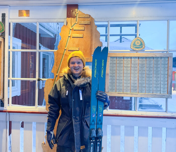 skier standing in front of a route map and commemmorative plaques