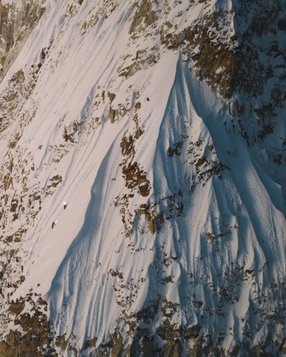 Two tiny climbers on a big face, progressing on vertiginous snow ramps and close to reaching the summit ridge.