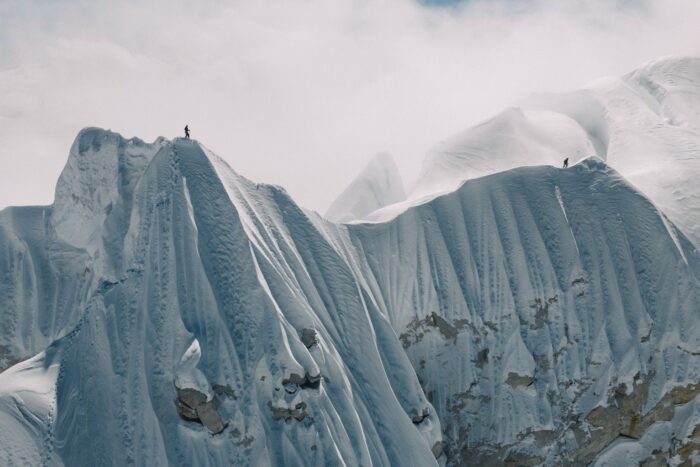 Two tiny climbers on different points of a sharp snow ridge.