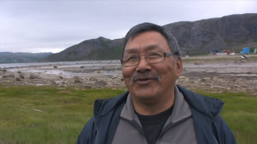 A smiling man standing outside, mountains and river in the background