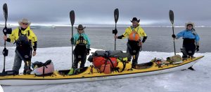 four kayakers stand on sea ice by a kayak