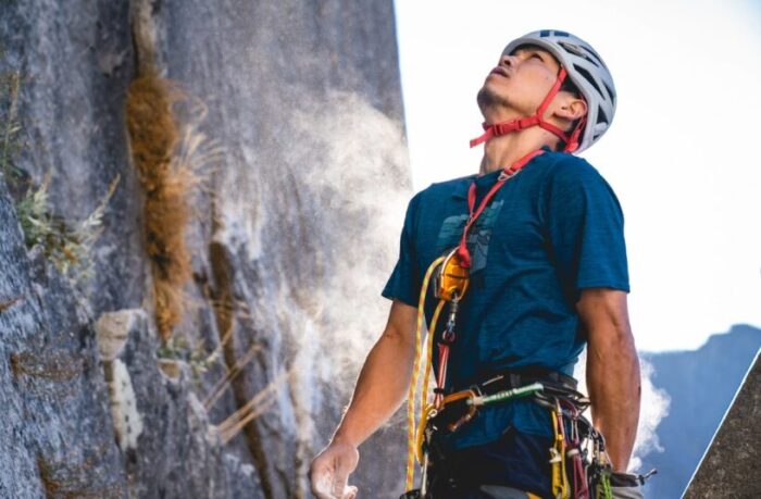 The ckimber looking up a rock face, with a gre-gri device on his chest to climb in solo-rope style, self-belaying.