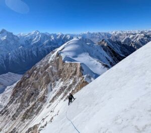 a climber at the end of the rope, traverses below snow ridge.