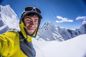 Selfie with anowy mountains in background on a sunny day. Jornet in light mountain clothes.