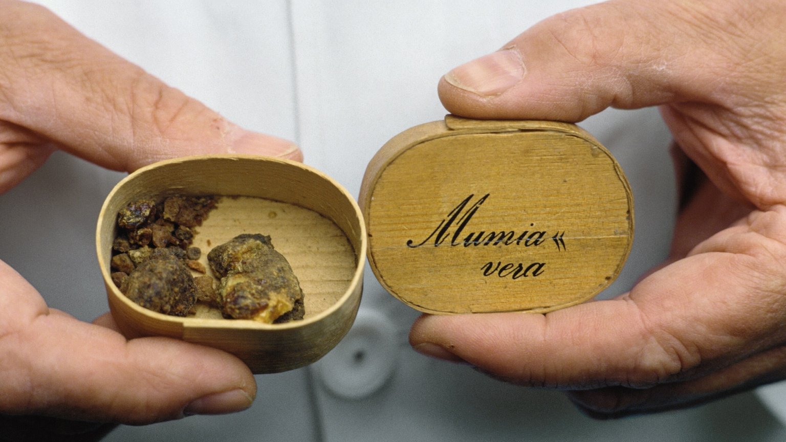 Hands holding a container labelled 'Mumia vera'