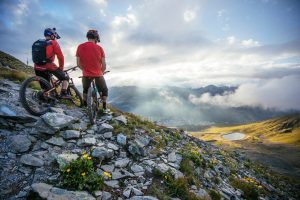 Two cyclists sit at the top of a mountain trail on a beautiful sunny day.