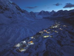 Many illuminated tents in the huge Base camp along the Khumbu glacier, surrounded by peaks, at dusk.