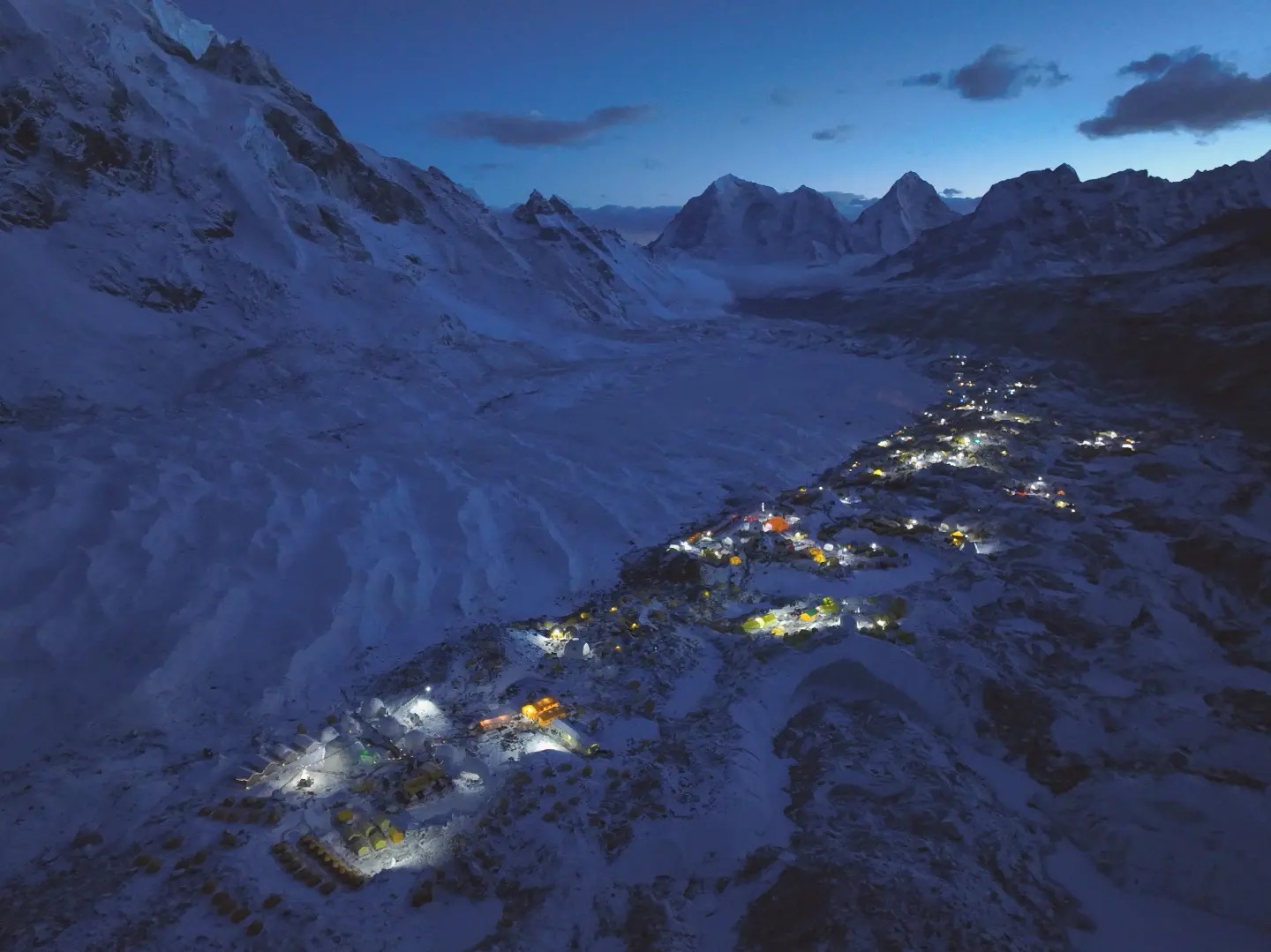 Many illuminated tents in the huge Base camp along the Khumbu glacier, surrounded by peaks, at dusk.