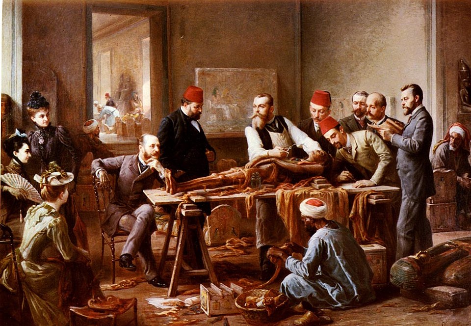 A group of people gathered around a table, where a mummy is being unwrapped
