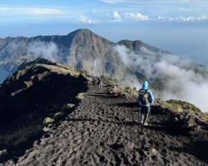A figure walking along a mountain trail with smoke