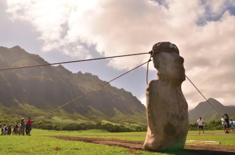 A group of 18 people use ropes to rock the moai statue from side to side.