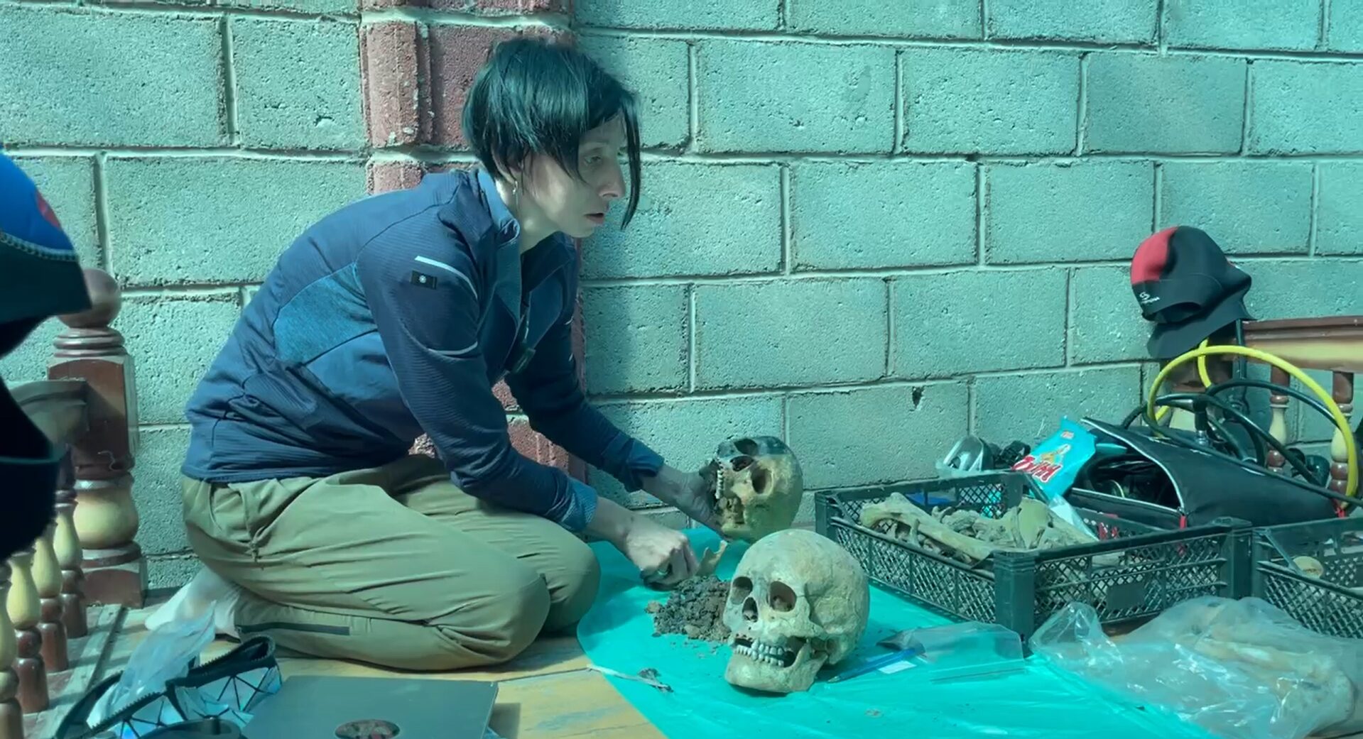 A woman holds one skull in her hand while another sits on the ground.