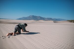An emaciated man crawling across dry ground under a blazing sun in a desert-like landscape.