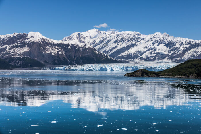 A large glacier runs into a glacial lagoon, with snow capped mountains the background