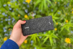 The author holds a black Anker power bank in front of a field of flowers.