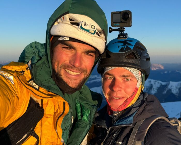 Close shot of the climbers on a summit at sunset/sunrise, with helmets and mountaineering jeckets.