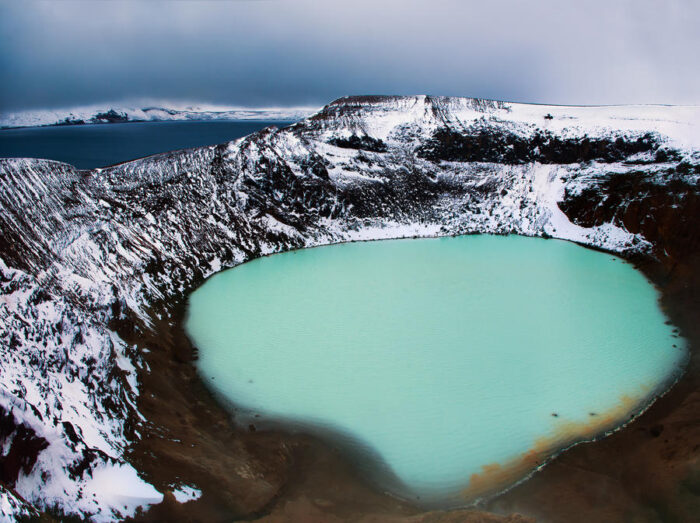 an aquamarine lake inside a snowy mountain caldera
