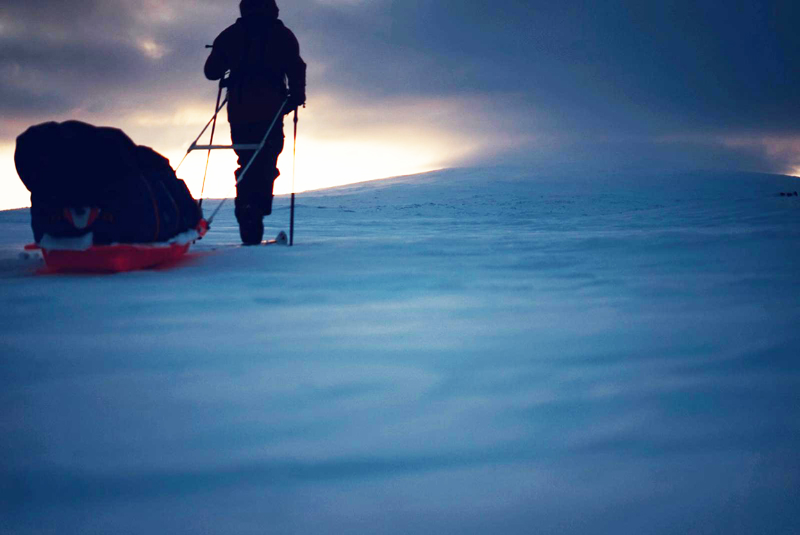 a skier pulling a sled into a sunset