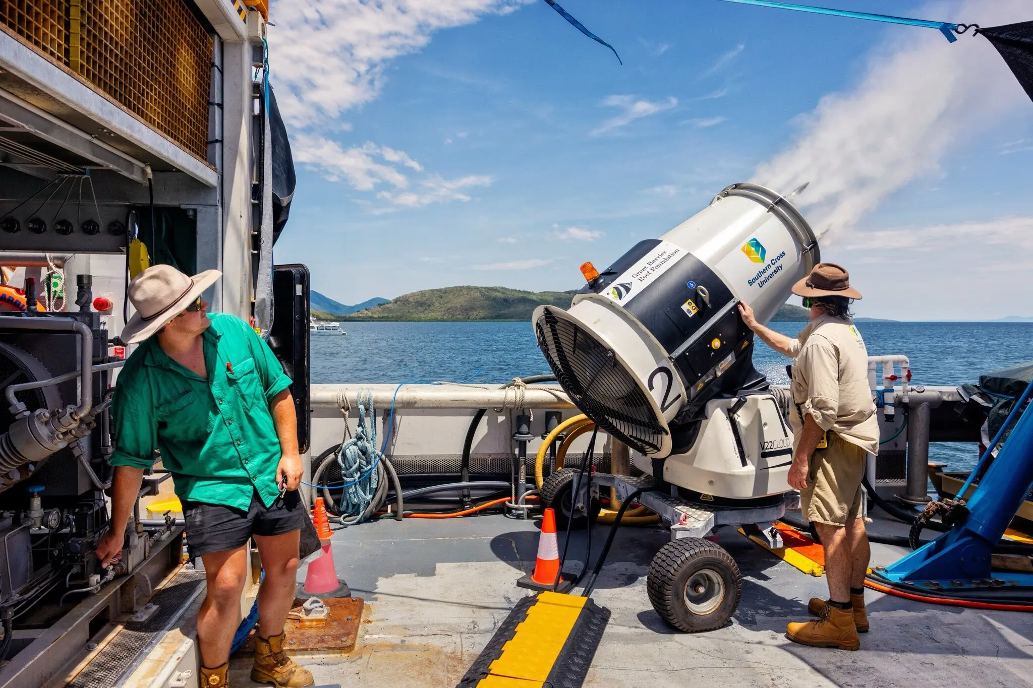 Two men man a strange aerosol gun on a ship.