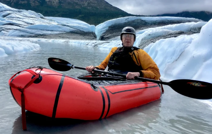 A man is pictured in a packraft holding a paddle surrounded by ice